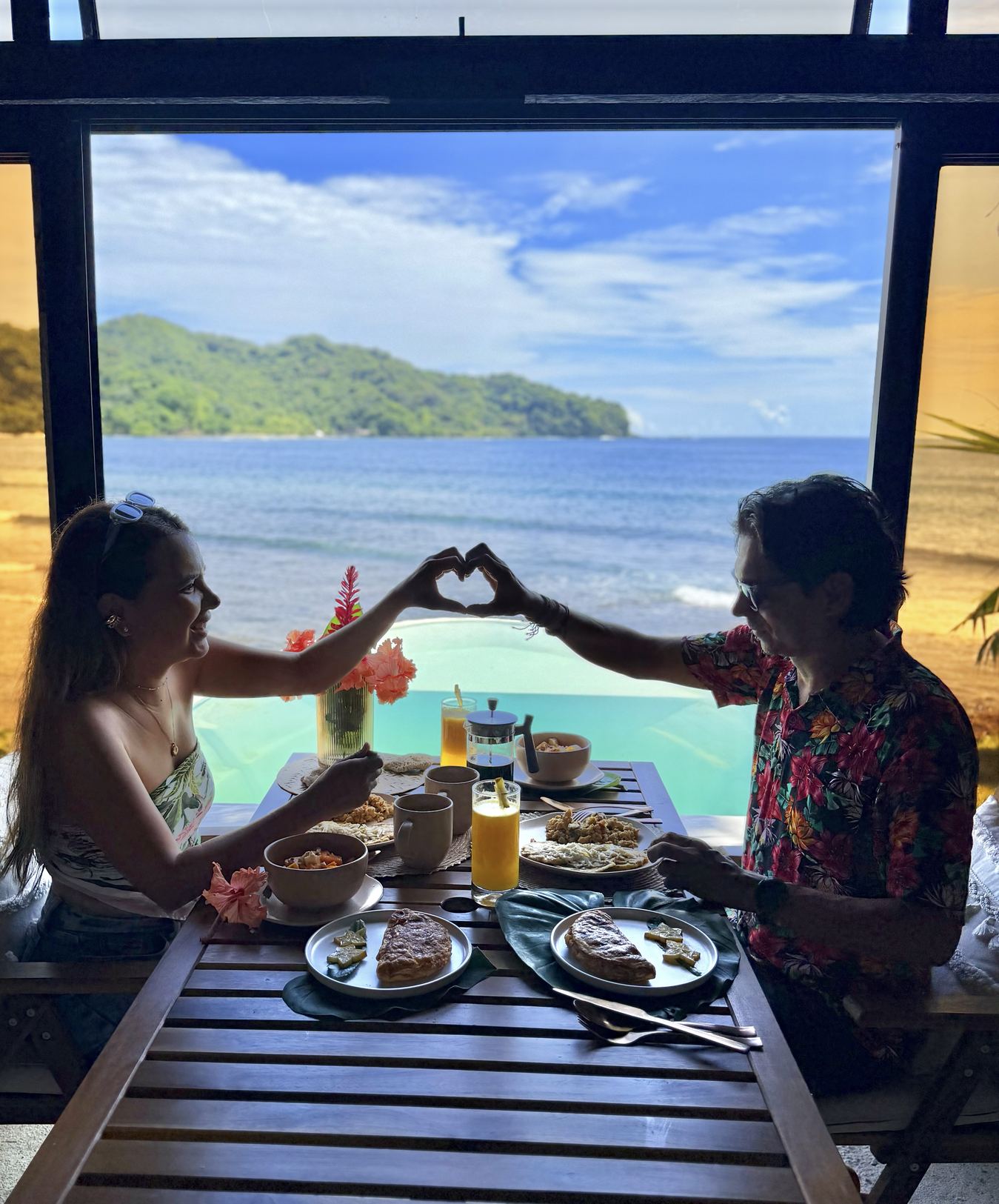 Pareja formando un corazón con las manos durante el desayuno frente al mar en Sapzurro